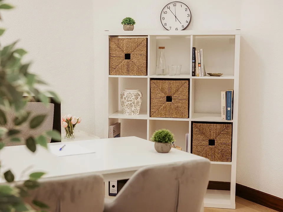 Sala de consulta de un centro de Psiconervión: mesa blanca con butacas tapizadas, un ramo de tulipanes y una estantería con libros y cestas de fibra